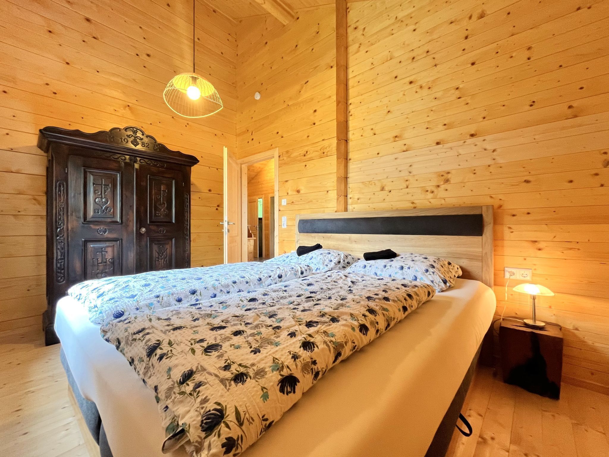 A wooden-paneled bedroom with a bed, a nightstand, and a hanging light fixture.
