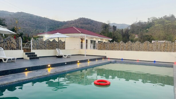 Une piscine avec deux cercles rouges, un espace de repos couvert et une vue sur une montagne.