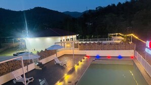 Un espace piscine agrémenté de chaises longues et de parasols, entouré d’une clôture en bois et bordé d’un bâtiment doté d’un toit en pente.