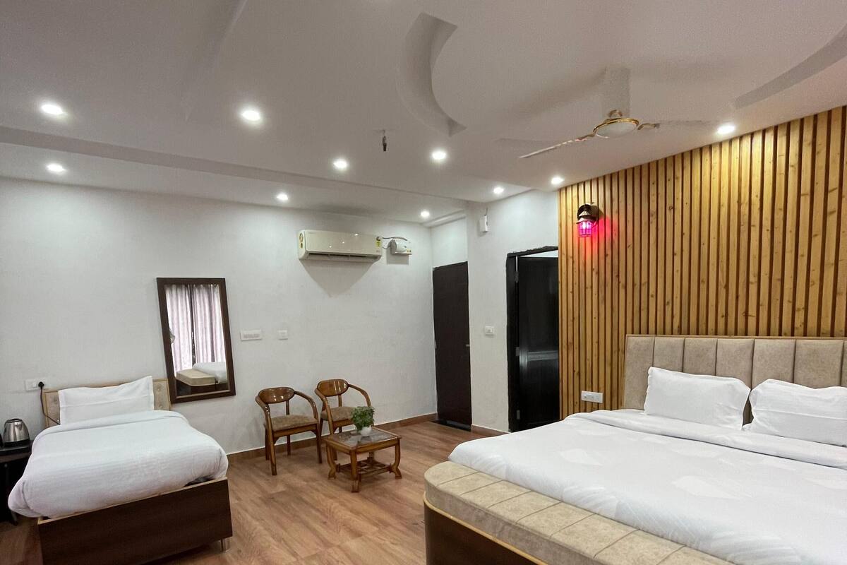 A modern hotel room with two beds, a wooden floor, a large mirror, a small table, and a ceiling light.