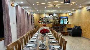 Une longue table à manger, dressée pour un repas, entourée de chaises en bois, agrémentée d’un arrangement floral central, et avec un bar en arrière-plan.