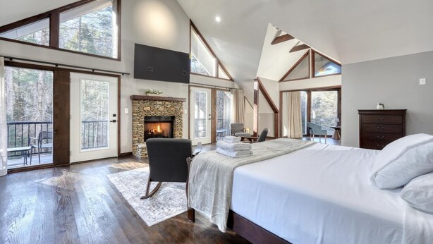 Een ruime slaapkamer met een groot bed, een stenen openhaard en een balkon met uitzicht op bomen.
