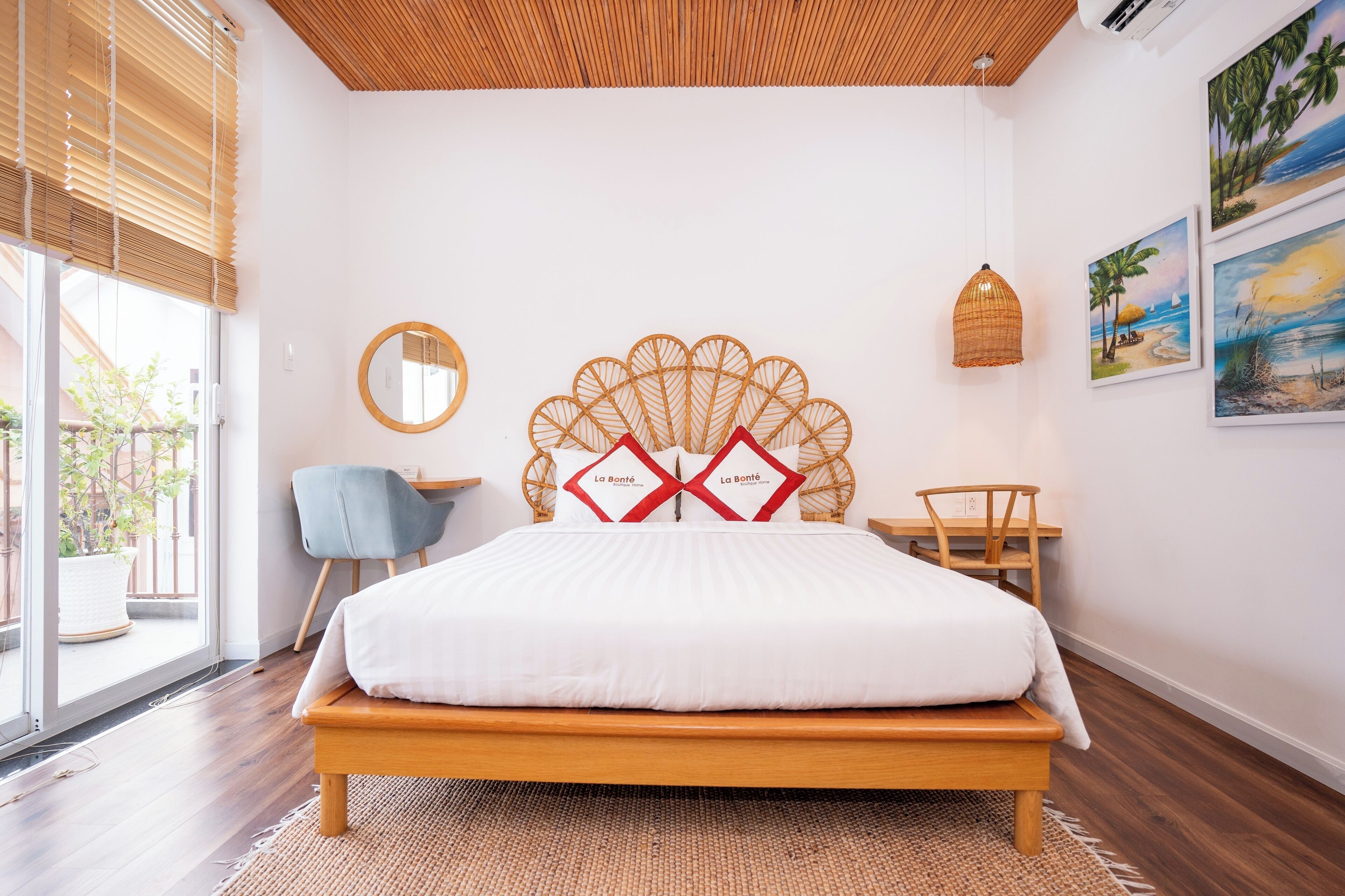 A bedroom with a wooden bed, a round mirror, a wicker headboard, and a view of the outdoors through large windows.