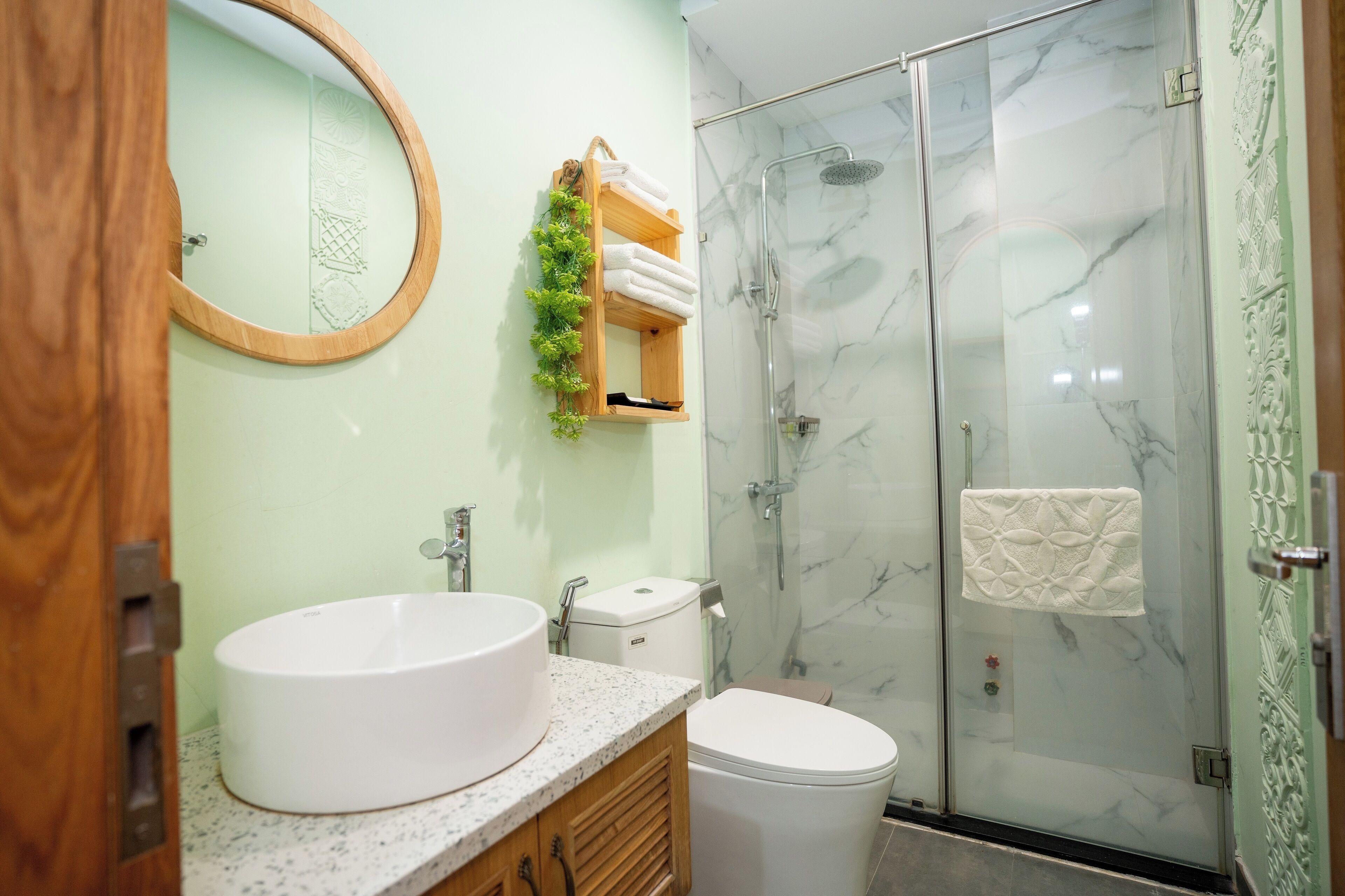 A bathroom with a round mirror, a sink, a toilet, and a glass-enclosed shower.