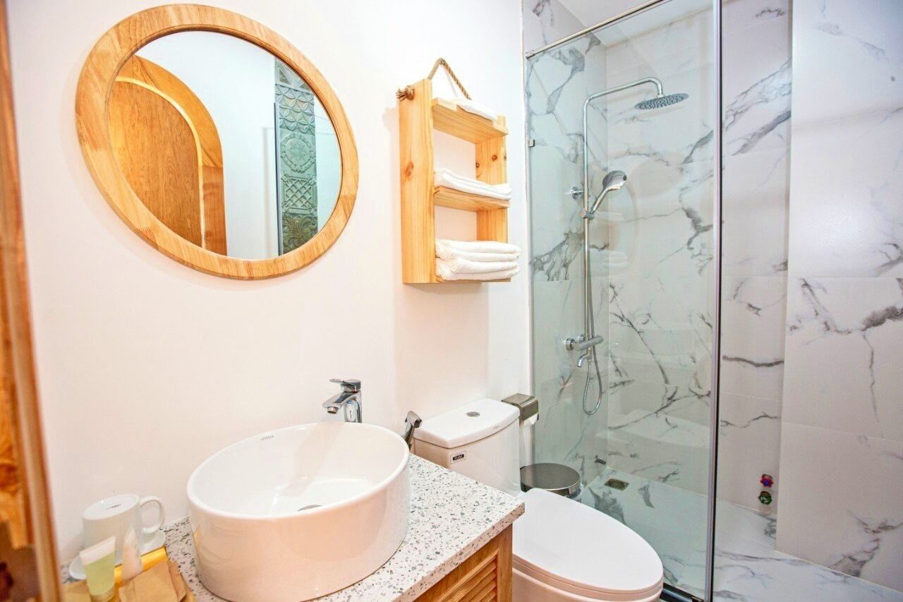 A bathroom with a round mirror, a white sink, a toilet, and a glass-enclosed shower.