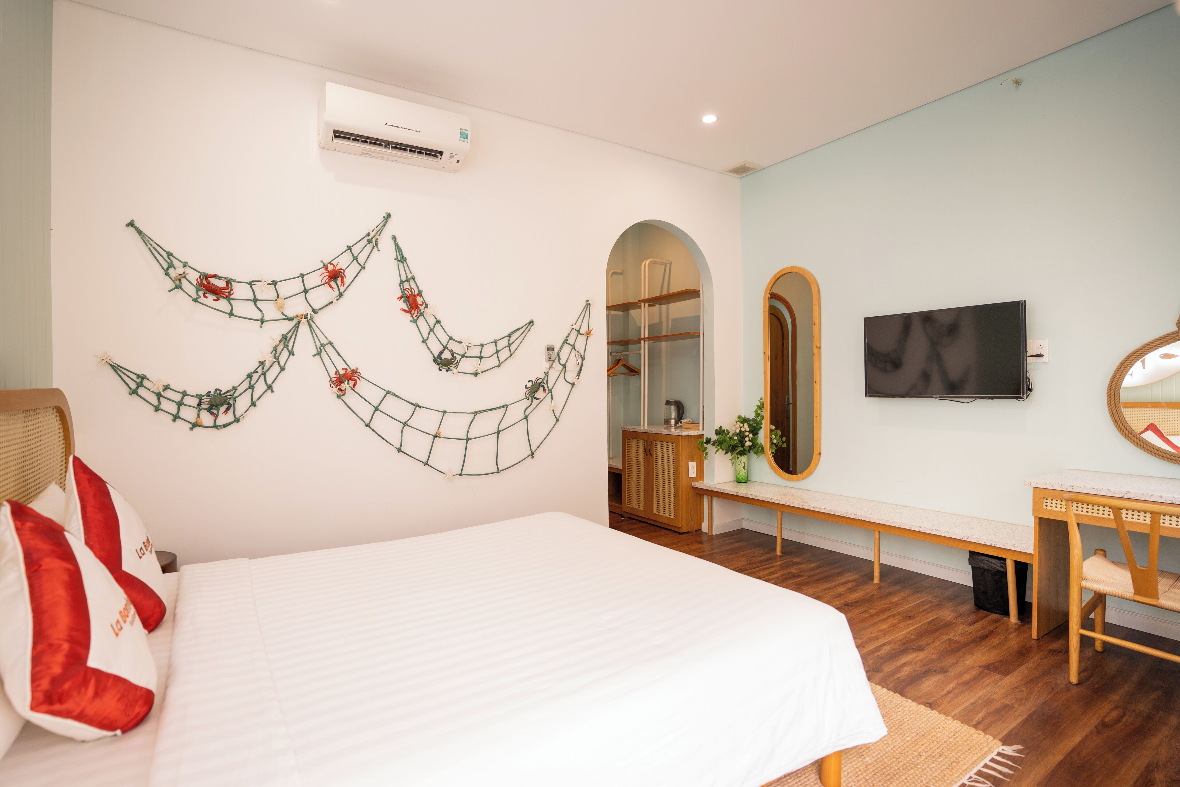 A bedroom with a bed, a TV, a mirror, a bench, and a wall decoration.