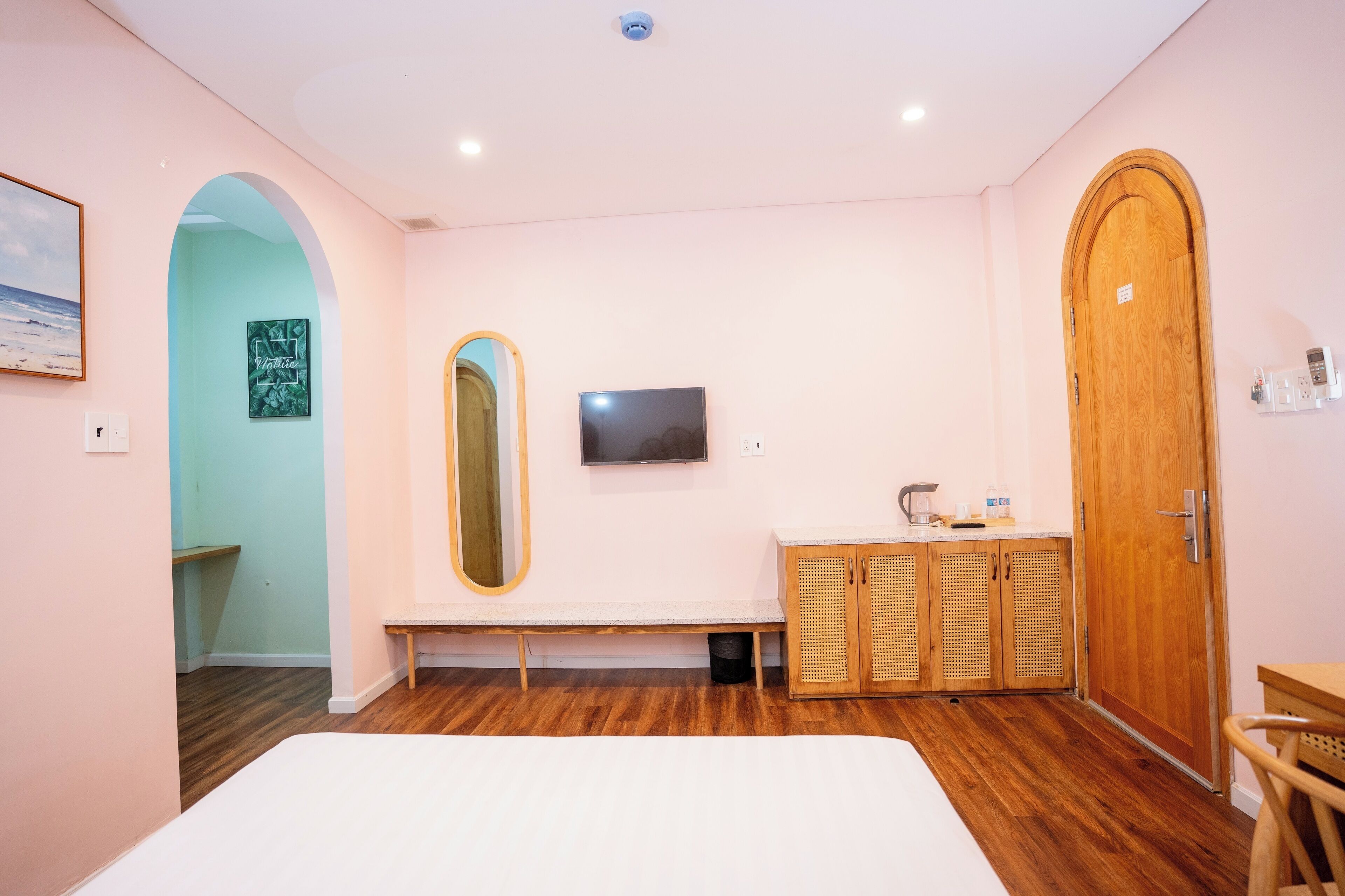 A bedroom with a large bed, a wooden wardrobe, a bench, a TV, and a mirror.
