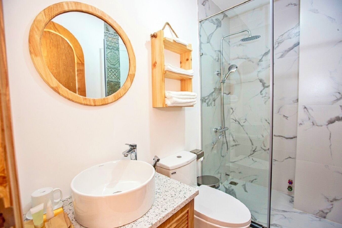 A bathroom with a round mirror, a sink, a toilet, and a glass-enclosed shower.