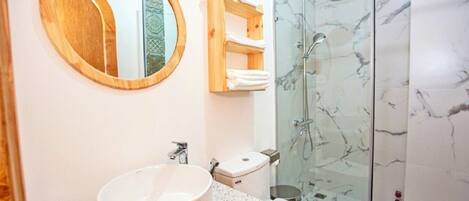 A bathroom with a round mirror, a sink, a toilet, and a glass-enclosed shower.