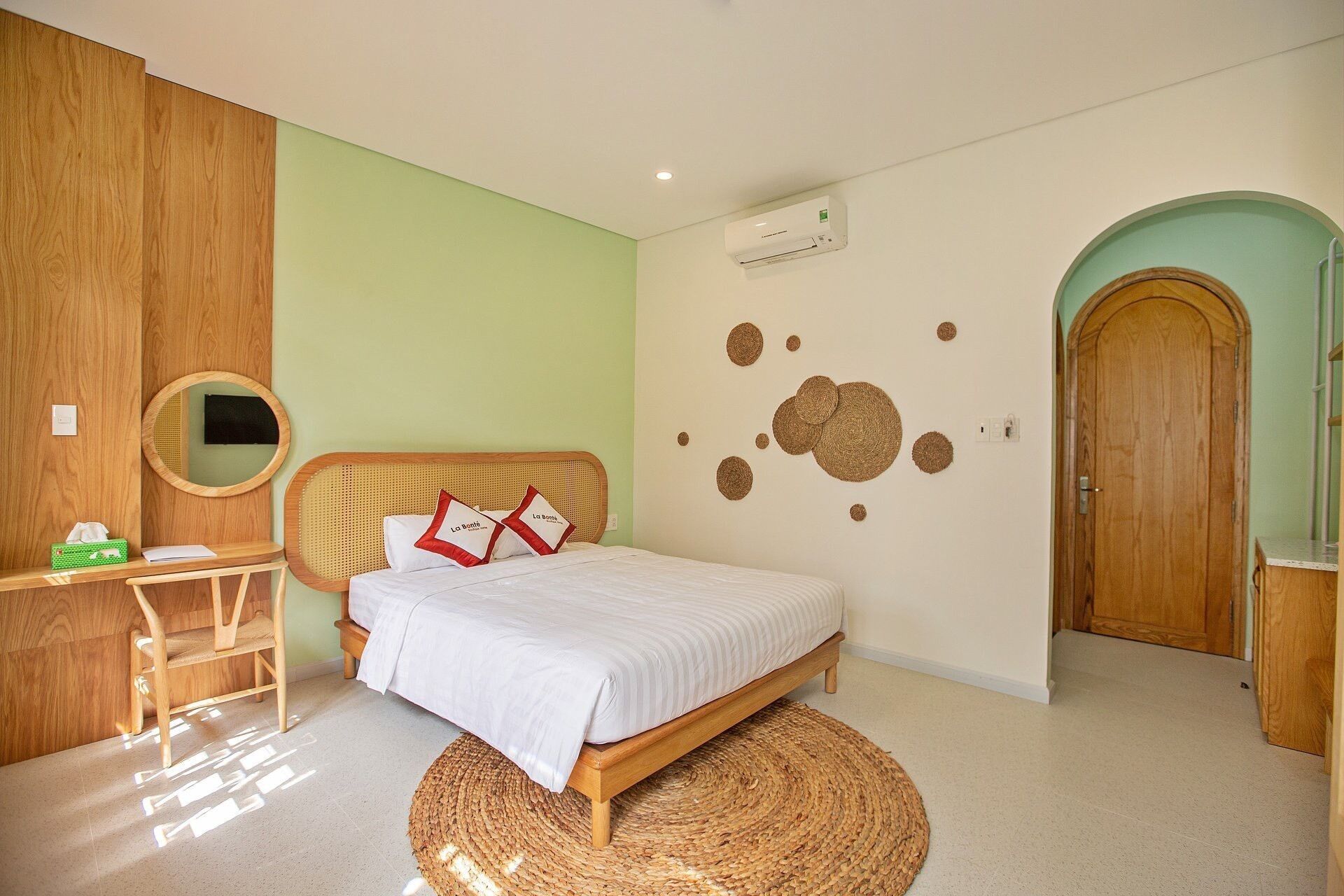 Une chambre à coucher avec un lit, un miroir rond, un bureau en bois et un tapis tissé.