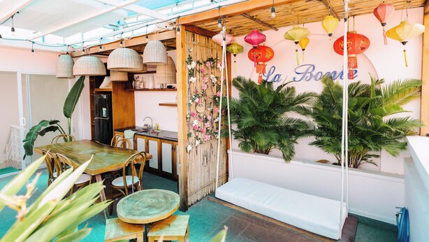 A cozy indoor dining area with a wooden table and chairs, a bench, and a wall with hanging lanterns. - La Bonté Boutique Home Vung Tau (Ho Chi Minh City)