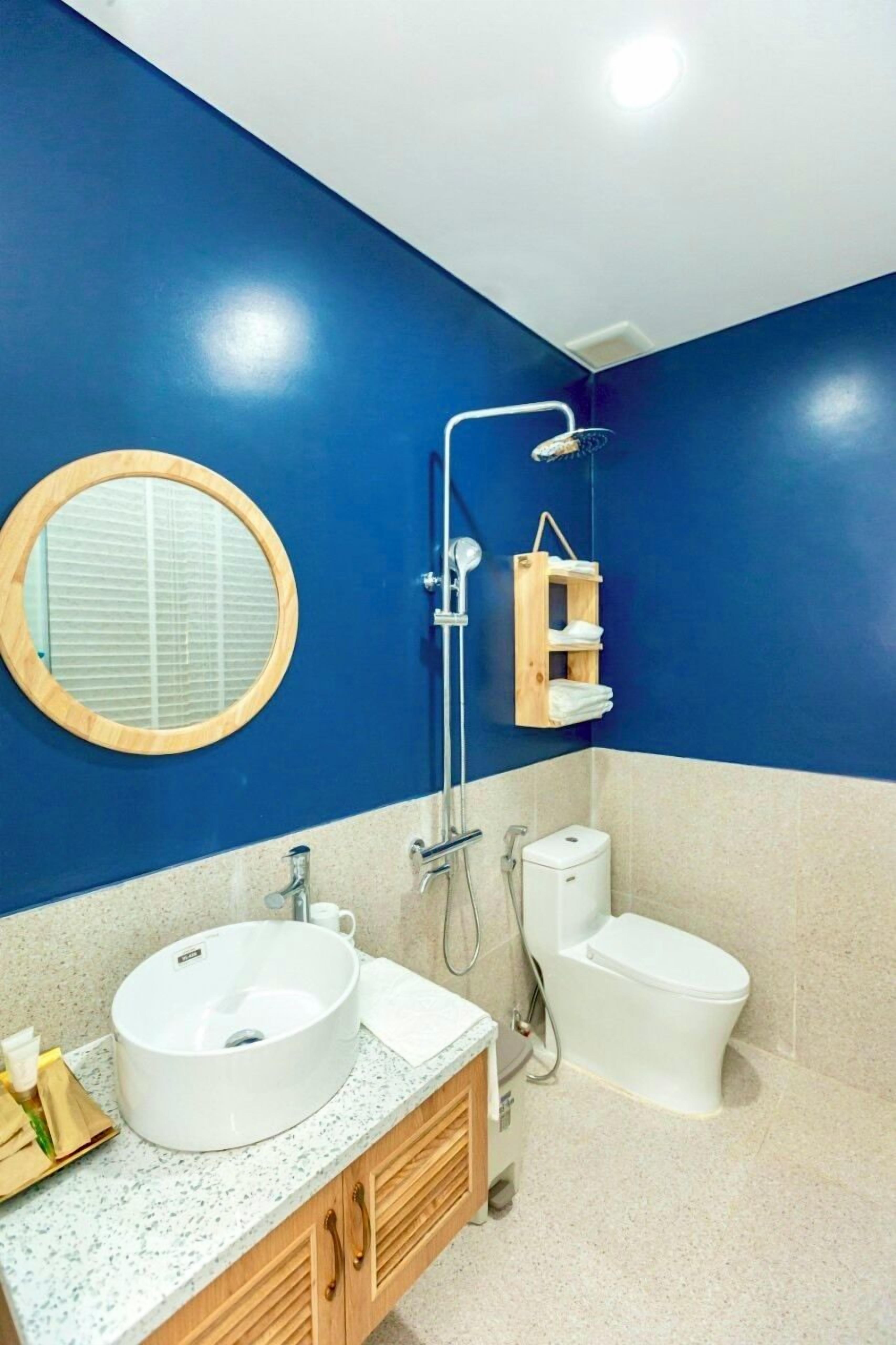 Un baño con pared azul, un espejo redondo, un lavabo, un inodoro y una ducha.