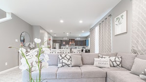 A modern living room with a sectional sofa, a coffee table, and a potted orchid plant. - Clovis Gem – 4BR, 3.5 Bath (Clovis)