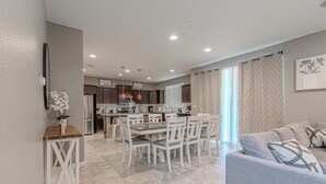 A modern kitchen with white cabinets, a dining table with chairs, and a grey sofa in the living area. - Clovis Gem – 4BR, 3.5 Bath (Clovis)