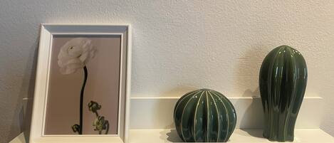 En hvid reol med et indrammet billede af en blomst, en grøn vase og en grøn keramikskål.