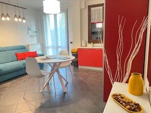 Ein modernes Wohnzimmer mit einem blauen Sofa, einem Esstisch und einer Küchenzeile mit roten Schränken.