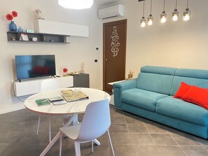 Ein modernes Wohnzimmer mit einer Couch, einem Esstisch mit Stühlen, einem Fernseher und Dekorationselementen.