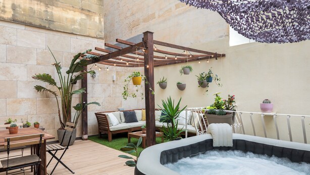 Un patio con mesa de madera, sillas, un sofá, un jacuzzi y plantas en macetas.