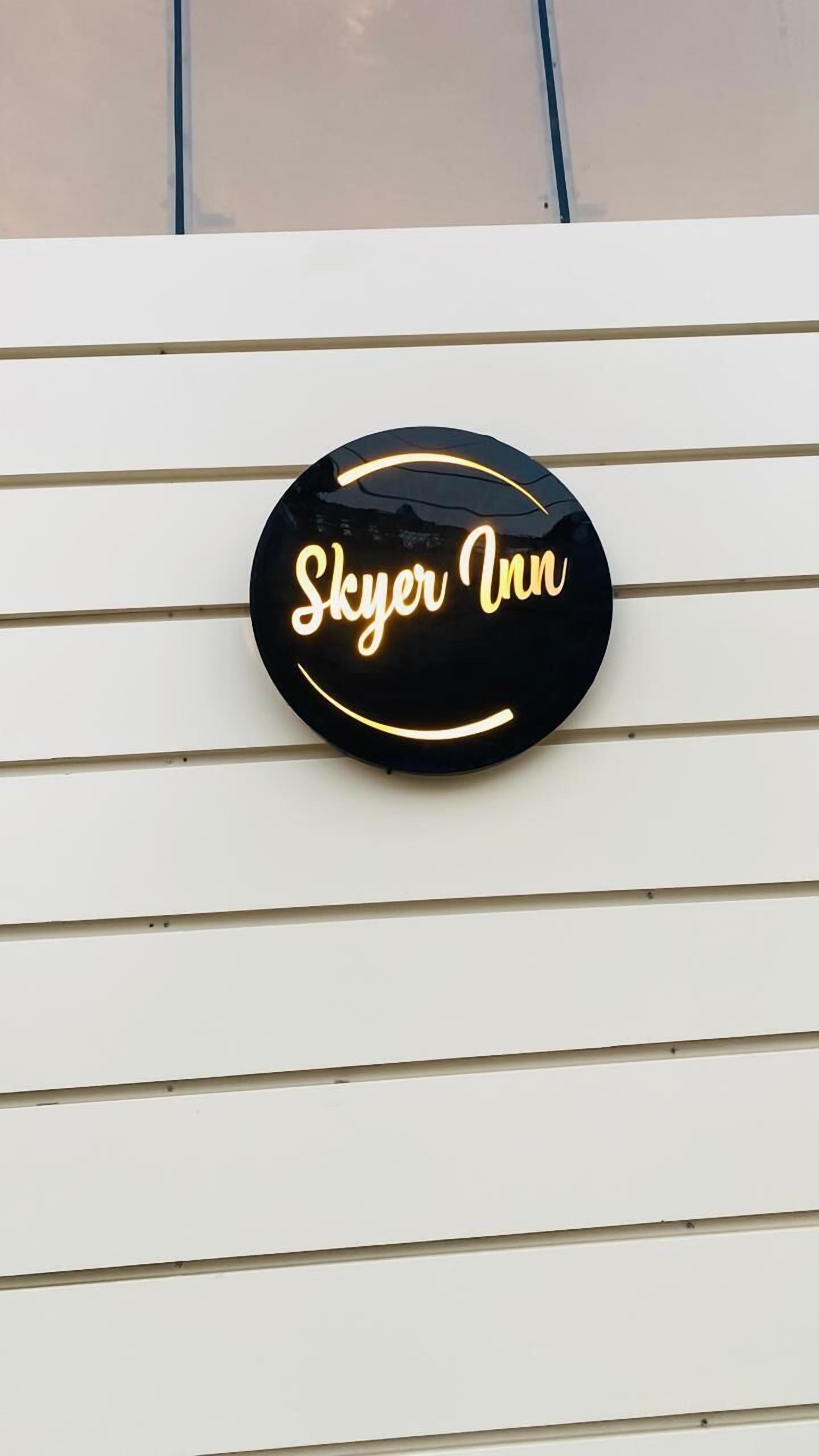 A black circular sign with the text "Skyer Inn" on a white wall with horizontal lines.