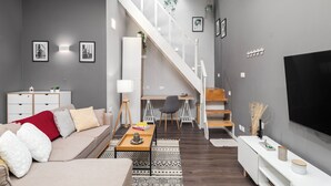 A modern living room with a sofa, coffee table, and TV. A staircase leads to a dining area with a table and chairs. - Sliema Pearl Luxury Apartment (Sliema)