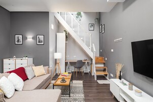 Una sala de estar moderna con un sofá, una mesa de centro y una televisión. Una escalera conduce a un comedor con una mesa y sillas.