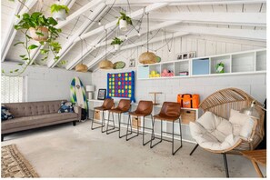 Une pièce de style « loft », avec un plafond haut, des poutres apparentes et différents types de sièges, notamment un canapé, des fauteuils et un fauteuil en osier.