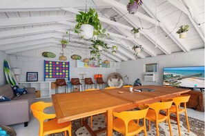 Une pièce spacieuse avec une table à manger en bois, des chaises orange, un canapé gris et un grand téléviseur diffusant une scène de plage.