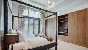 Ein Bett mit Baldachin, ein Fernseher auf einer Holzkommode, eine Lampe und ein Blick ins Freie durch große Fenster.