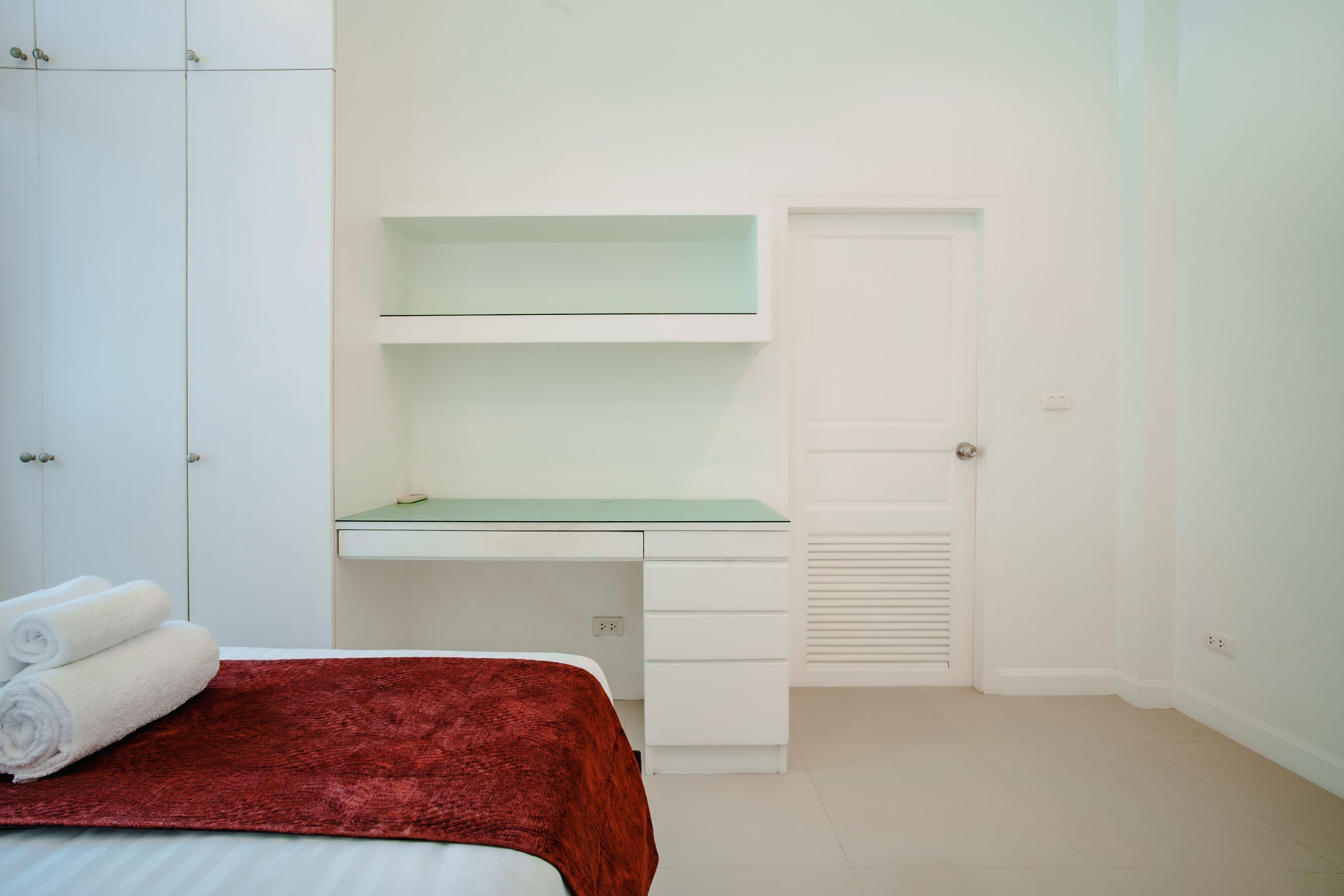 A bedroom with a bed, a desk with drawers, and a closet.