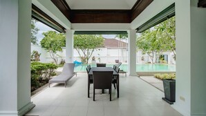 Eine überdachte Terrasse mit Pool, Gartenmöbeln und Blick auf die Umgebung.