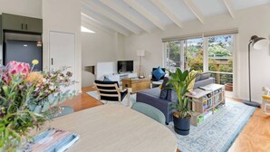 A modern living room with a sofa, a coffee table, a TV, and a dining area with a table and chairs. - The Balcony - pet friendly! (Jan Juc)