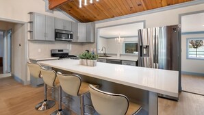 Una cocina moderna con una isla grande, taburetes de bar, electrodomésticos de acero inoxidable y techo de madera.