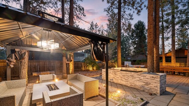Un patio al aire libre con zona de estar cubierta, una chimenea y una jardinera de piedra con plantas.