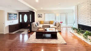 Ein geräumiges Wohnzimmer mit Holzboden, einem beigefarbenen Sofa, einem Couchtisch und einem Kamin.
