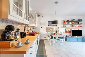 A modern kitchen with a wooden countertop, coffee maker, and a dining area with a table and chairs. - Blu Oltrelago: Leggiuno Lake Maggiore Apt w/ Shared Pool & Garden (Leggiuno)