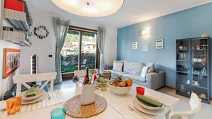 Un comedor con una mesa dispuesta para dos personas, una estantería, un sofá y vistas al exterior.