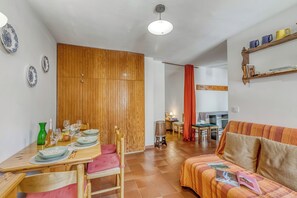 A dining area with a wooden table set for four, a sofa, and a kitchen in the background. - Gran Roc 23 (Sestriere)