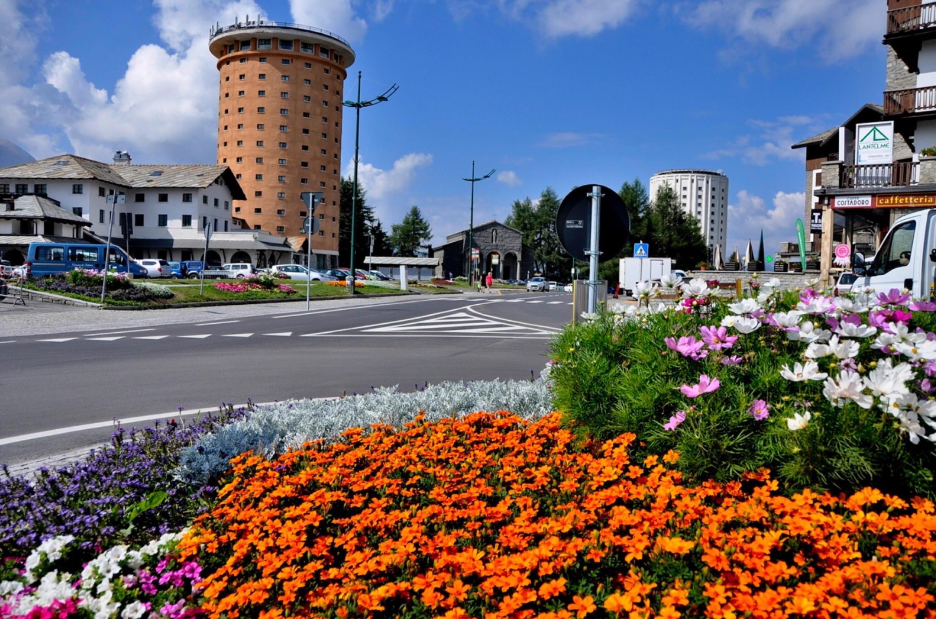 A street with a round building, a café, and a flower bed with various flowers.