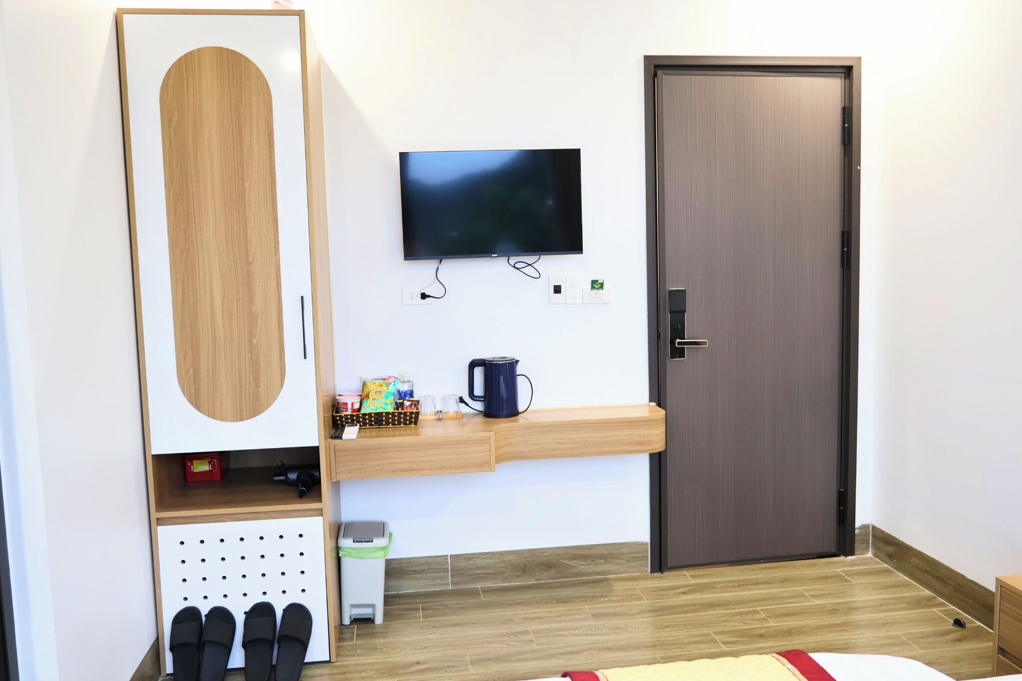 Habitación de hotel con un armario grande, un televisor montado, una mesita de centro pequeña y una puerta con picaporte.