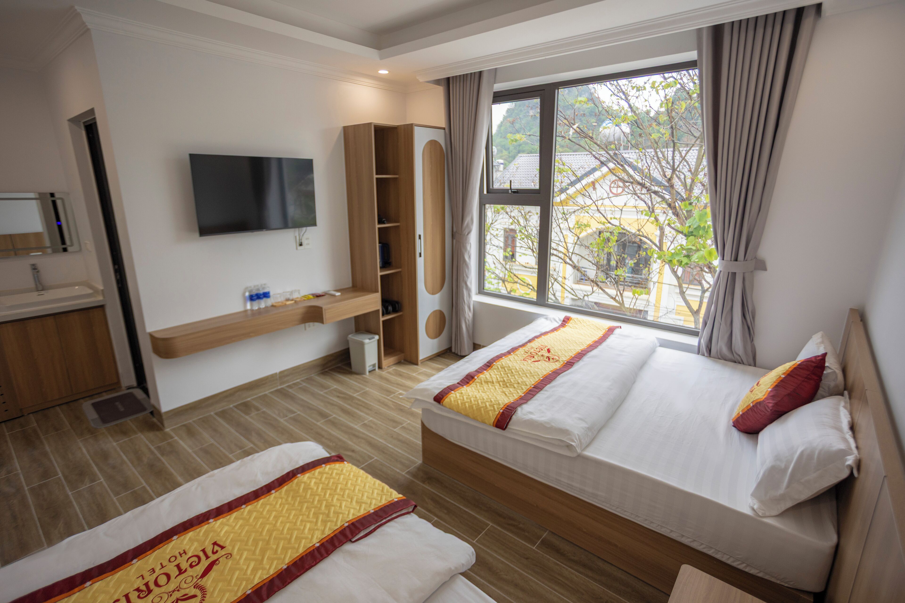 Habitación de hotel con dos camas, televisión, armario y ventana con vistas a edificios.