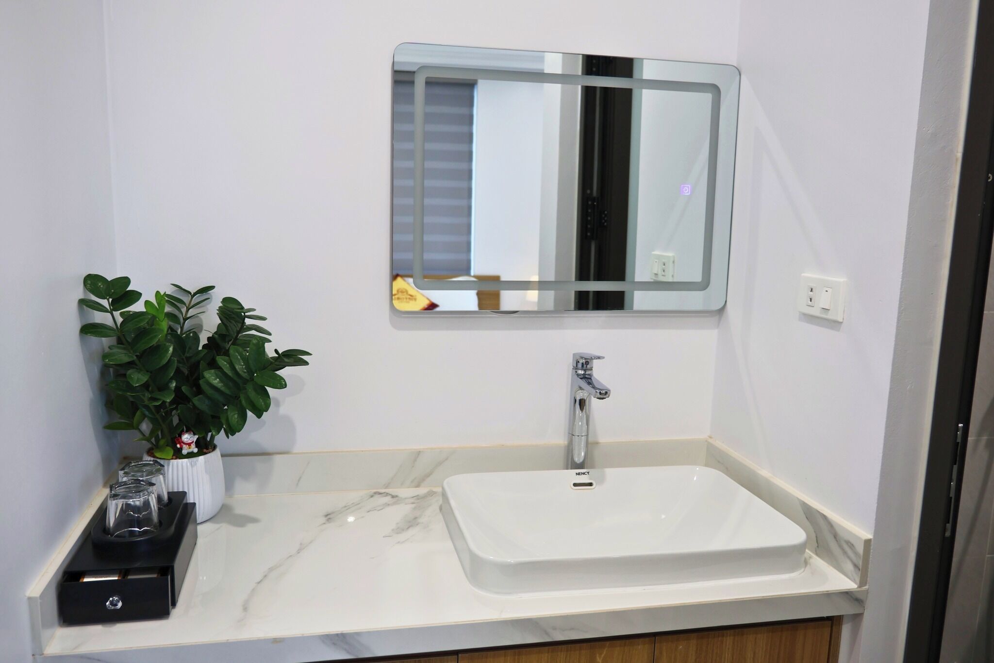 A bathroom with a white sink, a mirror, a potted plant, and a small cabinet.