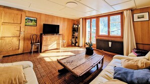 Een gezellige woonkamer met houten wanden, een televisie, een boekenkast en een groot raam met gordijnen.