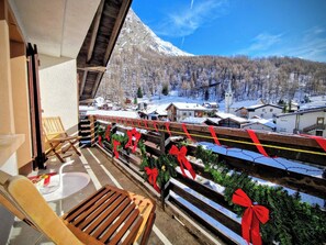 Un balcon avec des balustrades en bois, une chaise en bois et une vue sur une montagne enneigée et un village.