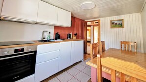 Een keuken met witte kastjes, een Bosch oven, een houten tafel en een zithoek met stoelen.