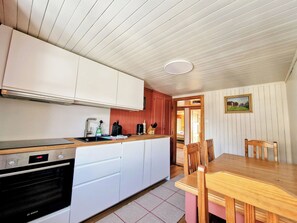 Una cocina con armarios blancos, un horno Bosch, una mesa de madera y una zona de comedor con sillas.