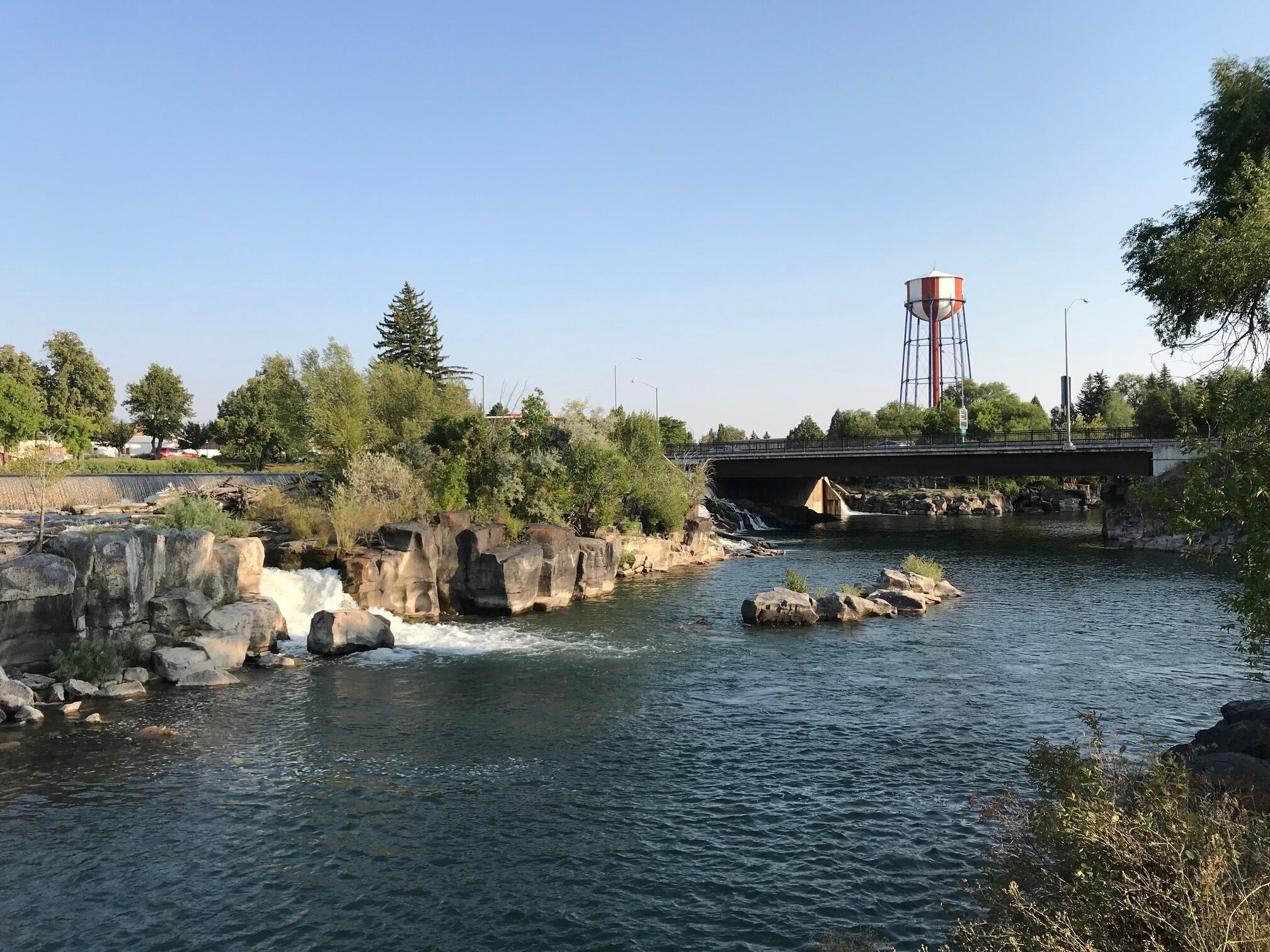 Une rivière avec une cascade, un pont et un château d’eau.