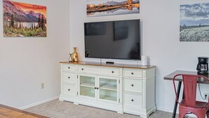 Habitación con televisión de pantalla plana sobre un mueble blanco, una silla roja y tres cuadros en la pared.