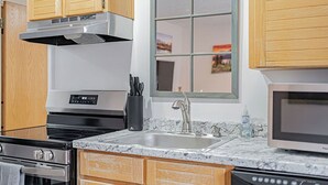 Una cocina moderna con estufa de acero inoxidable, pileta doble, armarios de madera y una ventana sobre la pileta.