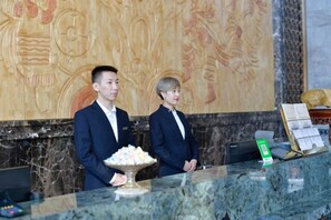 Dos personas de pie en la recepción, con un mostrador de mármol y una pared decorativa al fondo.