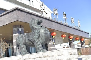 Un edificio con una gran estatua de bronce de un león, un cartel con caracteres chinos y farolillos rojos.